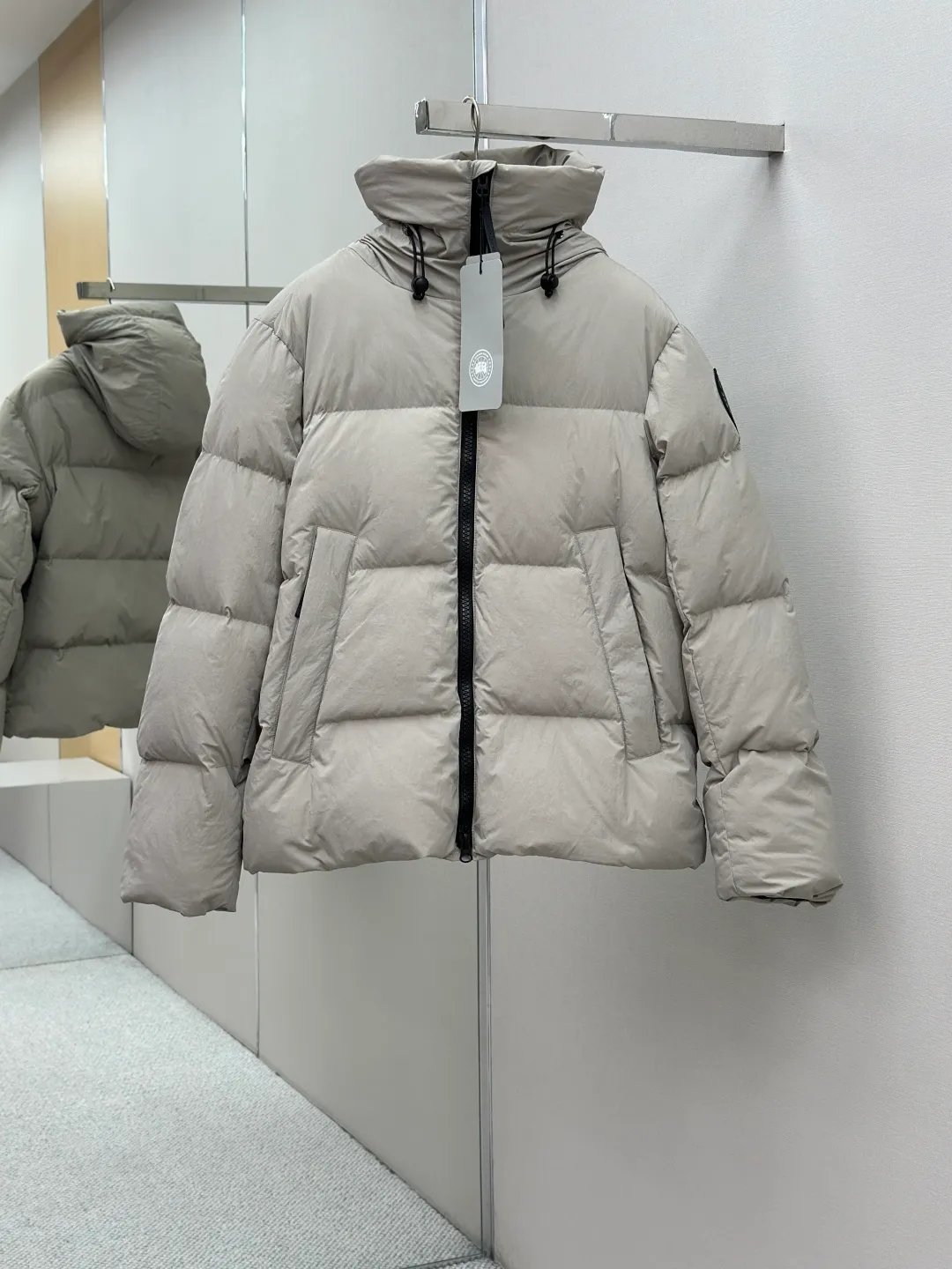 P1010 Canada Goose Black Label Badge Hooded Down Jacket (khaki) The high-quality filling is made of 90 national standard high-quality white duck down, selected high-loft velvet, weighing 240g, light and warm, with excellent temperature locking performance and good resilience. The fabric is woven with 400T high-count yarn. After special water-repellent treatment, the surface forms a lotus leaf effect - raindrops will slide down like beads, and snow particles will fall off when touched. The tear resistance reaches 200N (approximately 20kg load-bearing), the light gray matte texture breaks the stereotype of "outdoor clothing = hardcore", and the soft luster presents a high-end matte effect under urban neon lights, seamlessly switching scenes from ski resorts to CBD office buildings. The ribbon is woven with polyester as the base, and the brand letters are decorated on the ribbon through high-precision computer embroidery. The edges of the pattern are clear, the stitches are fine and even, and multiple layers of embroidery thread are stacked to enhance the three-dimensional effect. Precision thread reinforcement prevents linting and ensures the fluffy and resilient elasticity lasts as new. The embedded cuffs are three-dimensionally woven to form a "wavy" elastic structure, which forms natural folds when fitting the wrist, increasing the contact area with the skin, thus improving the windproof effect. At the same time, micro-velvet treatment is added to the inside of the cuffs, which feels like a second layer of skin and avoids friction on the skin from metal zippers or hard fabrics. Size:S-M-L-XL
